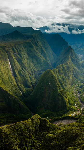 Aerial view of lush green volcanic mountains and a waterfall cascading down steep cliffs under a cloudy sky in La Reunion Nouvelle Aquitaine France. Aerial view of lush green volcanic mountains and a waterfall cascading down steep cliffs under a cloudy sky in La Reunion Nouvelle Aquitaine France.