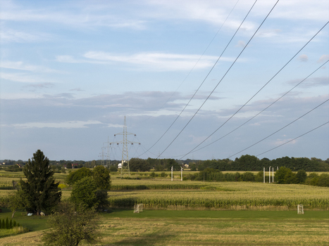 Aerial view of electric pylons and power lines stretching across rural corn fields and green meadows under a blue sky in Poland. Aerial view of electric pylons and power lines stretching across rural corn fields and green meadows under a blue sky in Poland.