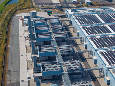 Aerial view of a large industrial datacenter facility featuring rows of cooling units and solar panels on the roof in The Netherlands. Aerial view of a large industrial datacenter facility featuring rows of cooling units and solar panels on the roof in The Netherlands.