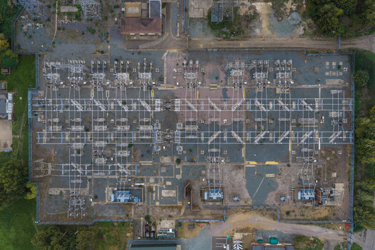 Aerial view of an electrical substation featuring high voltage transformers complex power lines and metal infrastructure set within a fenced area surrounded by trees in the United Kingdom. Aerial view of an electrical substation featuring high voltage transformers complex power lines and metal infrastructure set within a fenced area surrounded by trees in the United Kingdom.