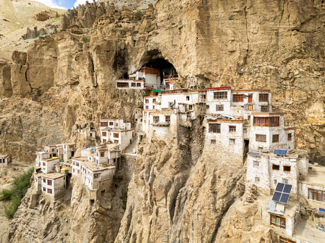 Aerial view of Phukthal Gompa monastery built into a dramatic cliffside with white buildings and solar panels in Phukthal Ladakh India.