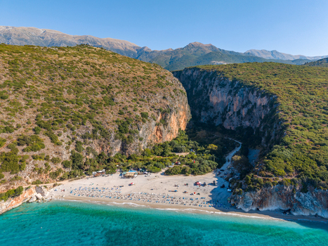 Aerial view of Gjipe Beach nestled within a deep canyon with turquoise waters sandy shore sun loungers and lush green vegetation Vlore County Albania. Aerial view of Gjipe Beach nestled within a deep canyon with turquoise waters sandy shore sun loungers and lush green vegetation Vlore County Albania.