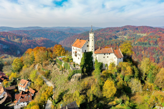 Aerial view of Gossweinstein Castle on a rocky hill surrounded by vibrant autumn foliage and rolling forested hills Gossweinstein Bayern Germany.