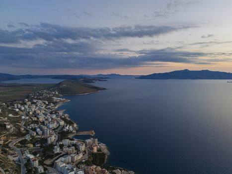 Aerial view of the coastal town of Saranda with its buildings nestled along the shoreline overlooking the Ionian Sea under a soft twilight sky in Saranda Vlore County Albania. Aerial view of the coastal town of Saranda with its buildings nestled along the shoreline overlooking the Ionian Sea under a soft twilight sky in Saranda Vlore County Albania.