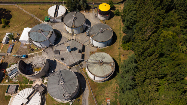 Aerial view of industrial storage tanks and facilities with some structures under maintenance or demolition surrounded by lush green trees in Milan Lombardy Italy. Aerial view of industrial storage tanks and facilities with some structures under maintenance or demolition surrounded by lush green trees in Milan Lombardy Italy.