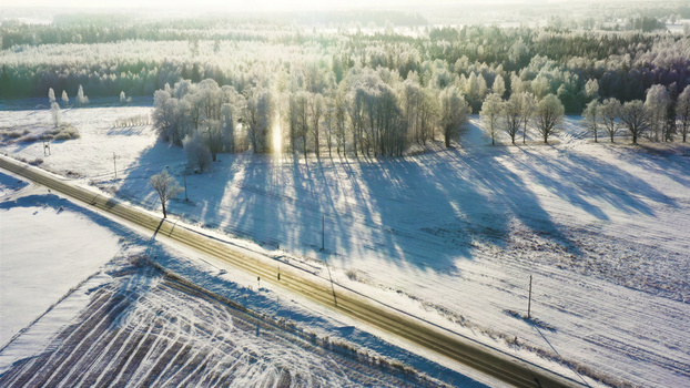 Aerial view of a snow covered landscape with a road cutting through surrounded by frost covered trees and fields under bright winter sunlight Latvija. Aerial view of a snow covered landscape with a road cutting through surrounded by frost covered trees and fields under bright winter sunlight Latvija.