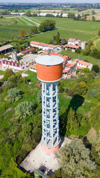 Aerial view of a tall cylindrical water tower with a brick facade and concrete support structure surrounded by rural fields and farm buildings in Mediglia Lombardy Italy. Aerial view of a tall cylindrical water tower with a brick facade and concrete support structure surrounded by rural fields and farm buildings in Mediglia Lombardy Italy.