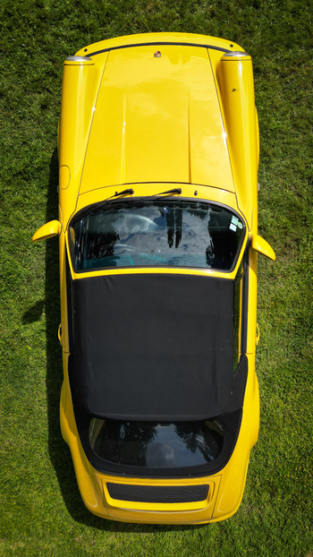 Aerial view of a yellow classic Porsche convertible parked on a lush green lawn under bright sunlight La Chapelle de Guinchay Bourgogne Franche Comte France.