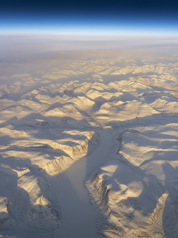 Aerial view of snow covered mountain peaks and a frozen river valley under a clear blue sky in Greenland. Aerial view of snow covered mountain peaks and a frozen river valley under a clear blue sky in Greenland.