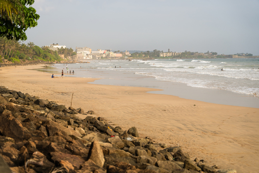 View of a sandy beach with people walking along the shore and waves crashing near the rocky coastline Galle Southern Province Sri Lanka.