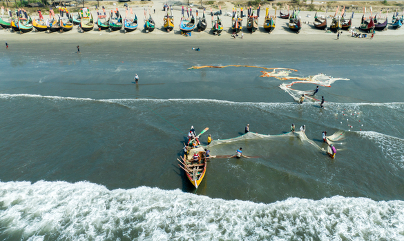 Aerial view of vibrant fishing boats lining the sandy beach as fishermen cast their nets into the sea at Cox s Bazar Chittagong Division Bangladesh. Aerial view of vibrant fishing boats lining the sandy beach as fishermen cast their nets into the sea at Cox s Bazar Chittagong Division Bangladesh.