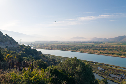 Aerial view of the Kanali i Vivarit flowing through lush wetlands and a flat valley with a wooden platform and hazy mountains in Vrine Vlore County Albania. Aerial view of the Kanali i Vivarit flowing through lush wetlands and a flat valley with a wooden platform and hazy mountains in Vrine Vlore County Albania.