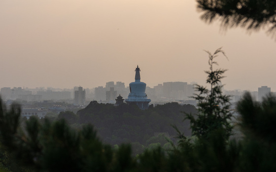 View of the White Dagoba in Beihai Park with the Beijing city skyline in the background framed by pine tree branches at sunset in Beijing Beijing China. View of the White Dagoba in Beihai Park with the Beijing city skyline in the background framed by pine tree branches at sunset in Beijing Beijing China.