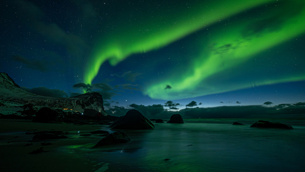 View of the aurora borealis illuminating the night sky above a rocky beach in Leknes Lofoten Norway.