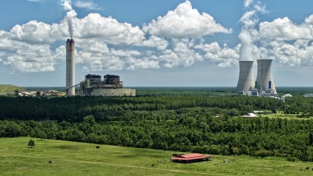 Aerial view of the Seminole Generating Station with its cooling towers and smokestack rising above the surrounding forest and green fields in Palatka Florida United States.