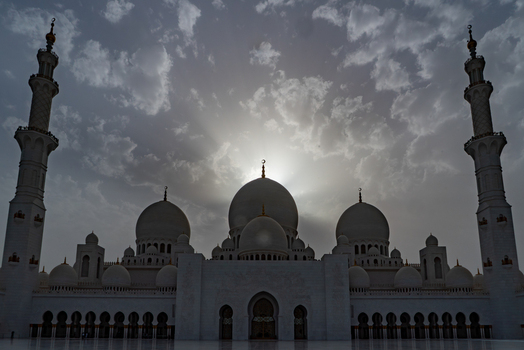 View of a grand mosque with white domes and tall minarets under a dramatic cloudy sky at sunset in Abu Dhabi Abu Dhabi United Arab Emirates. View of a grand mosque with white domes and tall minarets under a dramatic cloudy sky at sunset in Abu Dhabi Abu Dhabi United Arab Emirates.