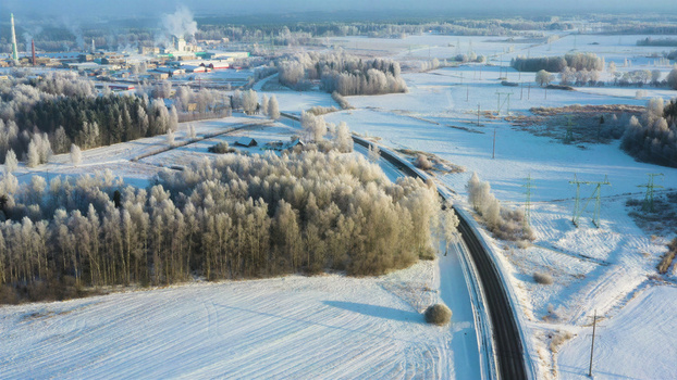 Aerial view of a snowy landscape with frost covered trees a winding road and an industrial facility with smoking chimneys in the distance Latvia. Aerial view of a snowy landscape with frost covered trees a winding road and an industrial facility with smoking chimneys in the distance Latvia.