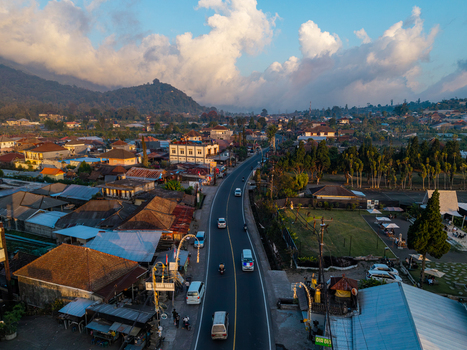 Aerial view of a road winding through the town with traditional houses lush greenery and distant mountains under a cloudy sky at sunset Kecamatan Sukasada Bali Indonesia. Aerial view of a road winding through the town with traditional houses lush greenery and distant mountains under a cloudy sky at sunset Kecamatan Sukasada Bali Indonesia.