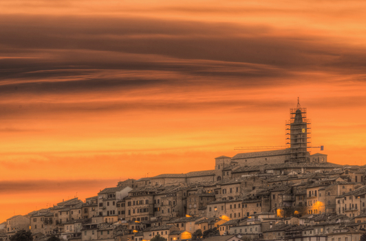 View of the historic town of Corridonia at sunset featuring a bell tower with scaffolding rising above stone rooftops under a vibrant orange sky in Corridonia Marche Italy. View of the historic town of Corridonia at sunset featuring a bell tower with scaffolding rising above stone rooftops under a vibrant orange sky in Corridonia Marche Italy.