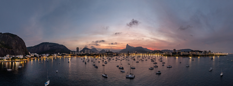 Aerial view of Botafogo Bay filled with sailboats at dusk with the city skyline and mountains under a colorful sunset sky Rio de Janeiro State of Rio de Janeiro Brazil.