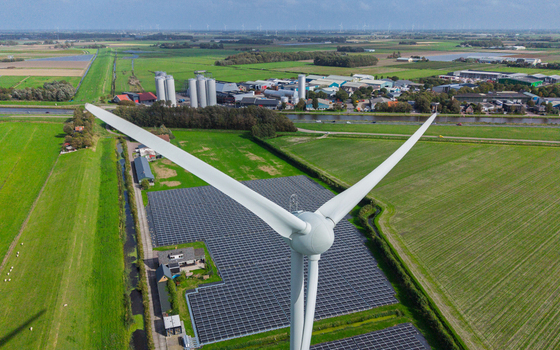 Aerial view of a large wind turbine standing next to a vast solar panel farm in the green rural landscape of t Zand North Holland Netherlands. Aerial view of a large wind turbine standing next to a vast solar panel farm in the green rural landscape of t Zand North Holland Netherlands.
