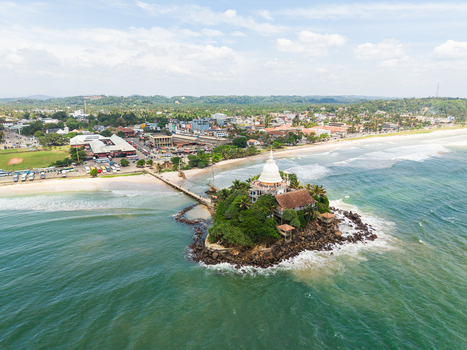 Aerial view of Parevi Duwa Temple on a small island connected by a bridge to the sandy beach and coastal town in Matara Southern Province Sri Lanka. Aerial view of Parevi Duwa Temple on a small island connected by a bridge to the sandy beach and coastal town in Matara Southern Province Sri Lanka.