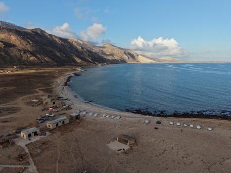 Aerial view of a tranquil coastline meets rugged mountains under a serene sky where the sandy beach hosts boats Dhi Hamri Socotra Yemen. Aerial view of a tranquil coastline meets rugged mountains under a serene sky where the sandy beach hosts boats Dhi Hamri Socotra Yemen.
