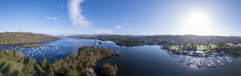 Aerial view of Windermere Lake shimmering under the sun dotted with sailboats and framed by lush green shores Windermere England United Kingdom. Aerial view of Windermere Lake shimmering under the sun dotted with sailboats and framed by lush green shores Windermere England United Kingdom.