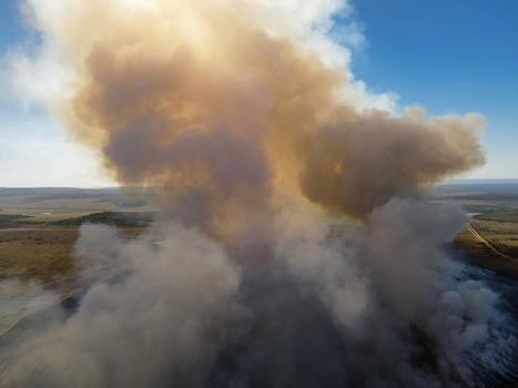 Aerial view of thick plumes of smoke rising from a wildfire over the vast savanna landscape under a clear blue sky in Waterberg District Municipality Limpopo South Africa.
