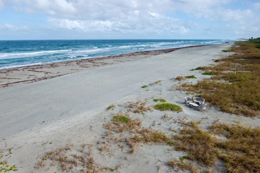 Aerial view of the sandy shoreline meeting the vast ocean with dunes covered in vegetation creating a contrast of textures and colors Jupiter Island Florida United States. Aerial view of the sandy shoreline meeting the vast ocean with dunes covered in vegetation creating a contrast of textures and colors Jupiter Island Florida United States.