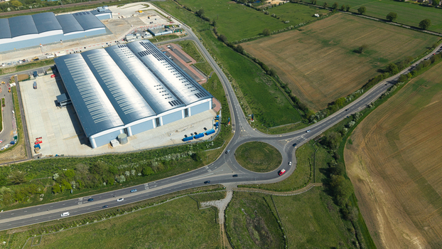 Aerial view of Symmetry Park industrial warehouse and a busy roundabout surrounded by green fields in Kettering England United Kingdom. Aerial view of Symmetry Park industrial warehouse and a busy roundabout surrounded by green fields in Kettering England United Kingdom.