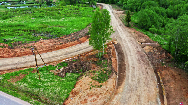 Aerial view of a dirt wind turbine maintenance road winding through a rural landscape with green grass trees and exposed earthworks in Latvija. Aerial view of a dirt wind turbine maintenance road winding through a rural landscape with green grass trees and exposed earthworks in Latvija.