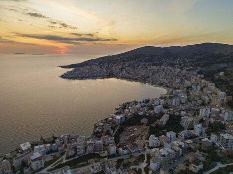 Aerial view of the coastal city of Saranda at sunset featuring dense urban buildings along the bay rolling hills and the calm Ionian Sea Saranda Vlore County Albania. Aerial view of the coastal city of Saranda at sunset featuring dense urban buildings along the bay rolling hills and the calm Ionian Sea Saranda Vlore County Albania.