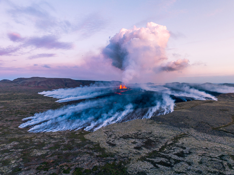 Aerial view of a volcanic eruption with glowing lava flows and thick plumes of smoke rising into the twilight sky over the rugged volcanic landscape of Iceland. Aerial view of a volcanic eruption with glowing lava flows and thick plumes of smoke rising into the twilight sky over the rugged volcanic landscape of Iceland.