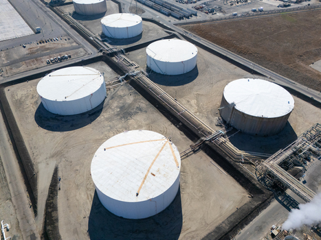 Aerial view of large white oil storage tanks and industrial piping infrastructure at a refinery facility in Carson California United States.
