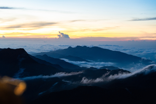 View of Adam s Peak mountain ridges silhouetted against a golden sunrise sky above a thick layer of clouds in Ratnapura Sabaragamuwa Province Sri Lanka. View of Adam s Peak mountain ridges silhouetted against a golden sunrise sky above a thick layer of clouds in Ratnapura Sabaragamuwa Province Sri Lanka.