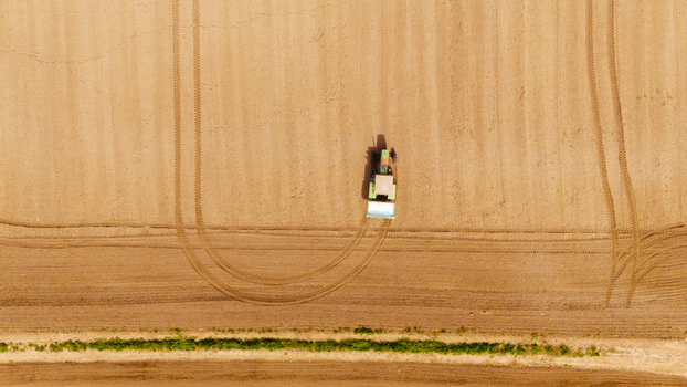 Aerial view of a tractor leaving curved tracks across a golden field edged with a strip of green Sremska Mitrovica Vojvodina Serbia. Aerial view of a tractor leaving curved tracks across a golden field edged with a strip of green Sremska Mitrovica Vojvodina Serbia.
