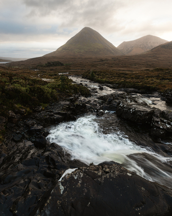 View of the Sligachan River flowing over dark rocks towards the conical peak of Glamaig mountain on the Isle of Skye Highland Council Scotland United Kingdom.