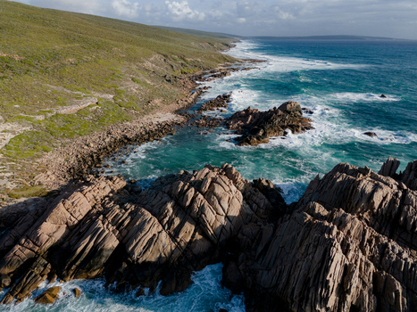 Aerial view of Sugarloaf Rock featuring jagged granite formations turquoise ocean waves crashing against the shore and lush coastal vegetation in Naturaliste Western Australia Australia.