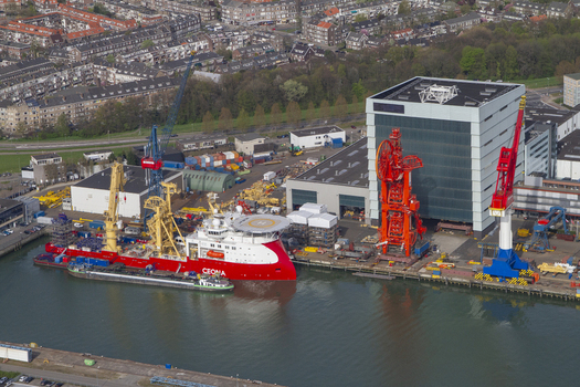 Aerial view of the industrial Rotterdam Harbour featuring a large red and white offshore vessel docked alongside heavy duty cranes and warehouse facilities in Rotterdam South Holland Netherlands. Aerial view of the industrial Rotterdam Harbour featuring a large red and white offshore vessel docked alongside heavy duty cranes and warehouse facilities in Rotterdam South Holland Netherlands.