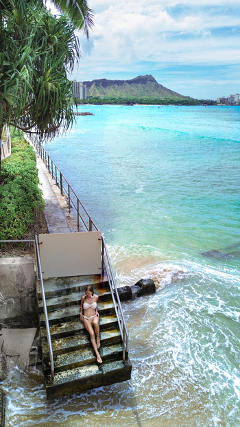 Aerial view of a woman in a bikini sitting on concrete stairs leading into the turquoise ocean with Diamond Head in the background in Honolulu Hawaii United States.