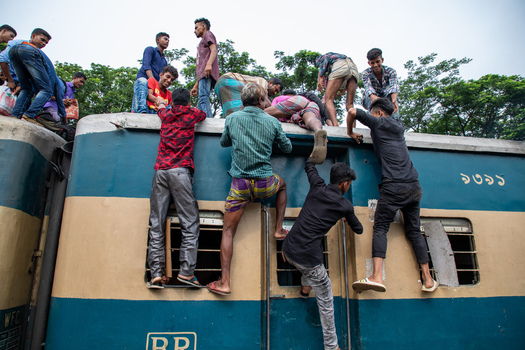 Dhaka Bangladesh 14 June 2018 View of people climbing onto the roof of a crowded train at Airport Railway Station with lush green trees in the background. Dhaka Bangladesh 14 June 2018 View of people climbing onto the roof of a crowded train at Airport Railway Station with lush green trees in the background.