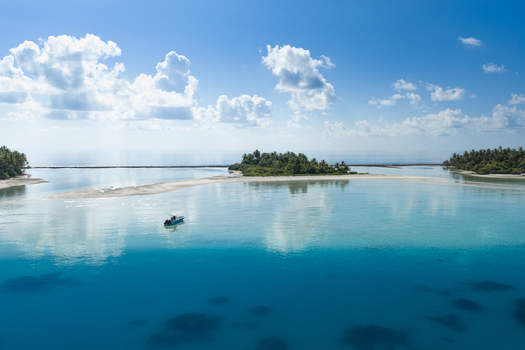 Aerial view of a small tropical island with lush palm trees surrounded by crystal clear turquoise water and a small boat in the lagoon Kudahuvadhoo Dhaalu Atoll Maldives. Aerial view of a small tropical island with lush palm trees surrounded by crystal clear turquoise water and a small boat in the lagoon Kudahuvadhoo Dhaalu Atoll Maldives.
