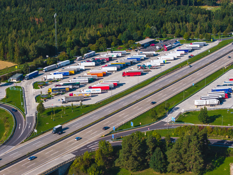 Aerial view of Logistikzentrum Allhaming with numerous semi trucks parked in rows next to a highway interchange surrounded by green forest in Allhaming Oberosterreich Austria. Aerial view of Logistikzentrum Allhaming with numerous semi trucks parked in rows next to a highway interchange surrounded by green forest in Allhaming Oberosterreich Austria.