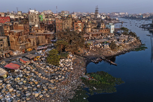 Aerial view of Buriganga River featuring dense urban architecture riverside waste collection with numerous sacks and small wooden boats on the water in Dhaka Dhaka Division Bangladesh. Aerial view of Buriganga River featuring dense urban architecture riverside waste collection with numerous sacks and small wooden boats on the water in Dhaka Dhaka Division Bangladesh.
