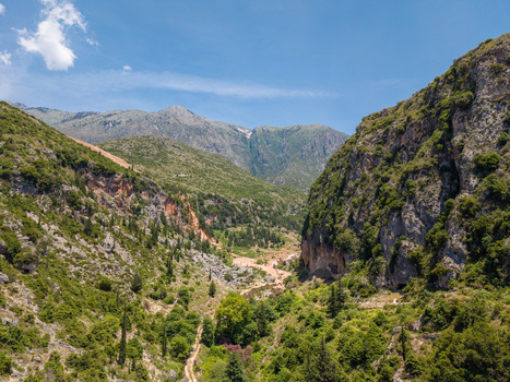 Aerial view of a lush green valley nestled between steep rocky mountains under a clear blue sky in Dhermi Vlore County Albania.