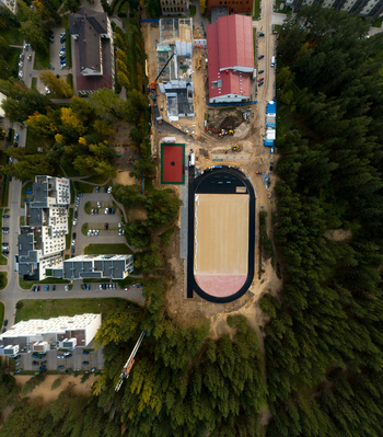 Aerial view of a construction site featuring a new sports field with a running track surrounded by residential buildings and dense forest in Latvia. Aerial view of a construction site featuring a new sports field with a running track surrounded by residential buildings and dense forest in Latvia.