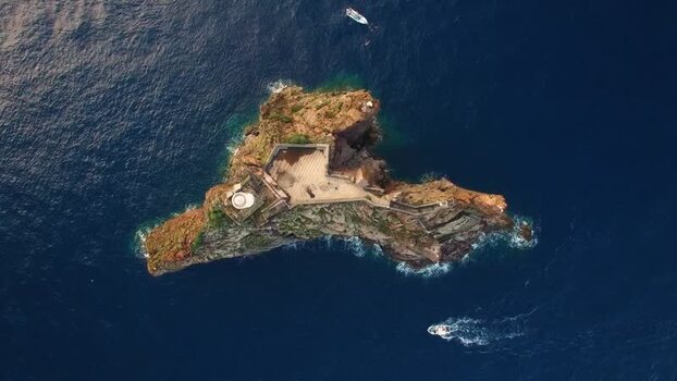 Aerial view of rocky islet with stone structure and lighthouse Italy.