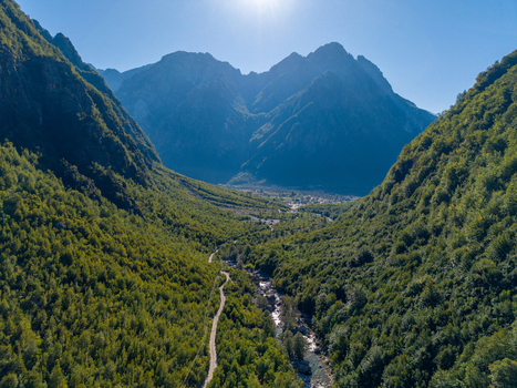 Aerial view of the lush green valley and winding river leading towards the Blue Eye Theth surrounded by towering mountains in Theth Shkoder County Albania. Aerial view of the lush green valley and winding river leading towards the Blue Eye Theth surrounded by towering mountains in Theth Shkoder County Albania.