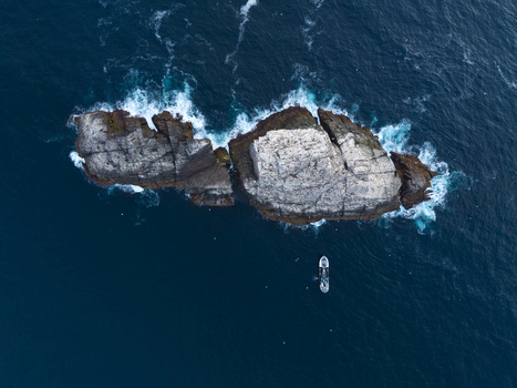 Aerial view of Sule Stack surrounded by deep blue ocean waters with a small boat navigating nearby in Scotland United Kingdom. Aerial view of Sule Stack surrounded by deep blue ocean waters with a small boat navigating nearby in Scotland United Kingdom.